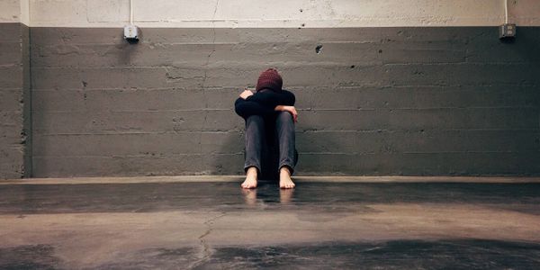 A person sitting against a wall with their knees up and head down.