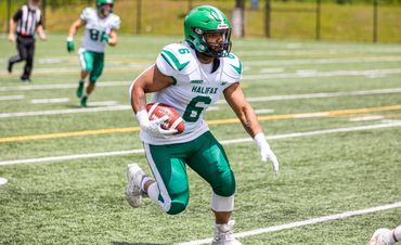 Football player in green and white uniform running with the ball on the field.