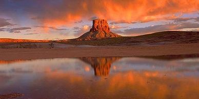 Butte rock formation reflecting in still water during sunset.