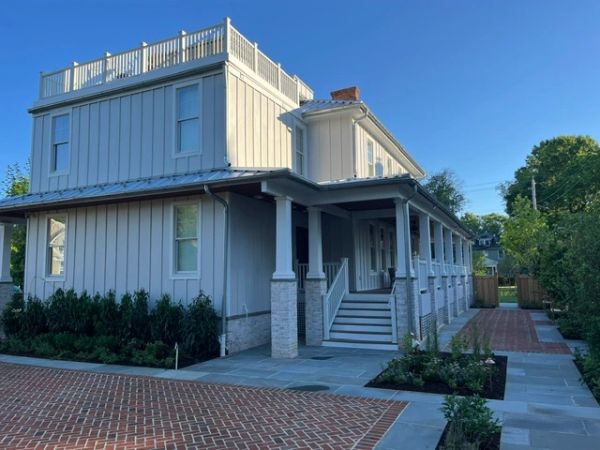 Modern white house with a wraparound porch and brick driveway.