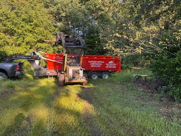 Compact loader in front of a red dumpster at a wooded property.