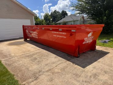 Red roll-off dumpster placed on a concrete driveway beside a garage.