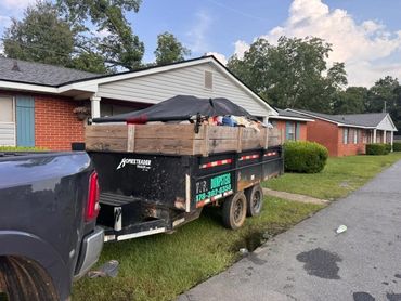 Loaded black dump trailer with wooden side panels parked behind a pickup truck.