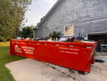 Red Mobi Dumpsters roll-off dumpster beside a gray house.
