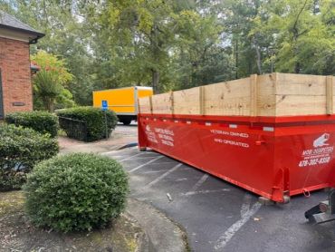 Red dumpster with wooden panels in a parking area.