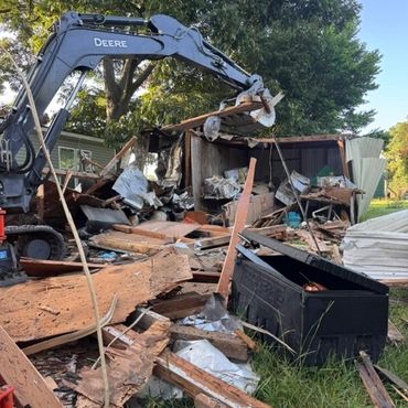 Excavator demolishing a wooden structure in a yard.