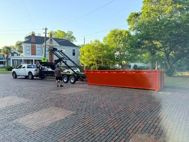 Red roll-off dumpster behind a white pickup truck with the trailer lift raised.