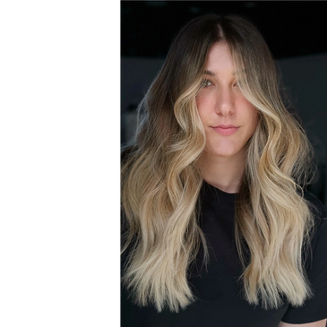 Woman with long, wavy blonde hair and dark roots.