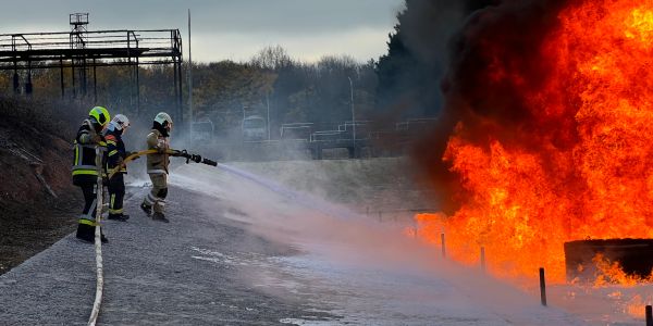 Firefighters spray water on a large fire outdoors.