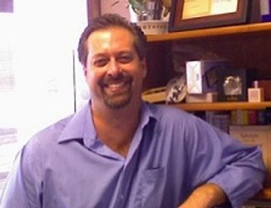 Smiling man in a blue shirt sitting in a cozy office.