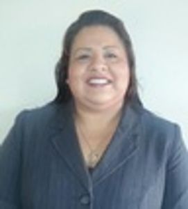 Smiling woman in a dark blazer poses for a photo against a plain background.