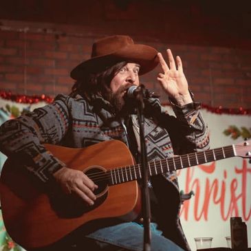 Man playing guitar and singing on stage wearing a cowboy hat.