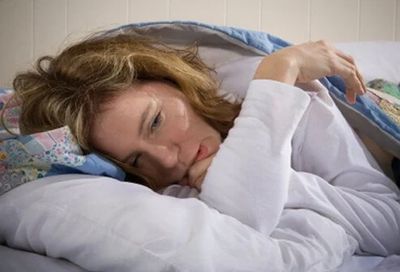 Woman suffering in bed with the ravages of ME/CFS (post-exertional malaise)