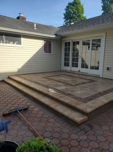 A clean, tiled patio with three steps leading to glass doors on a sunny day.