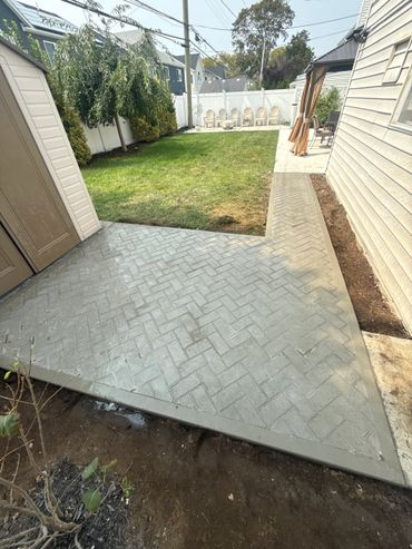 Recently poured concrete patio with a herringbone pattern in a backyard.