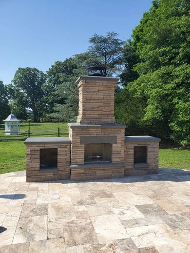 Outdoor stone fireplace with a chimney on a tiled patio under clear blue sky.