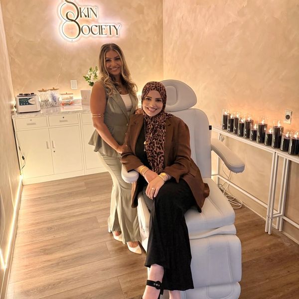 Two women smiling inside a cozy skincare clinic with warm lighting.