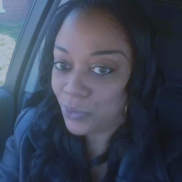 Woman with long dark hair sitting in a car, looking at the camera.