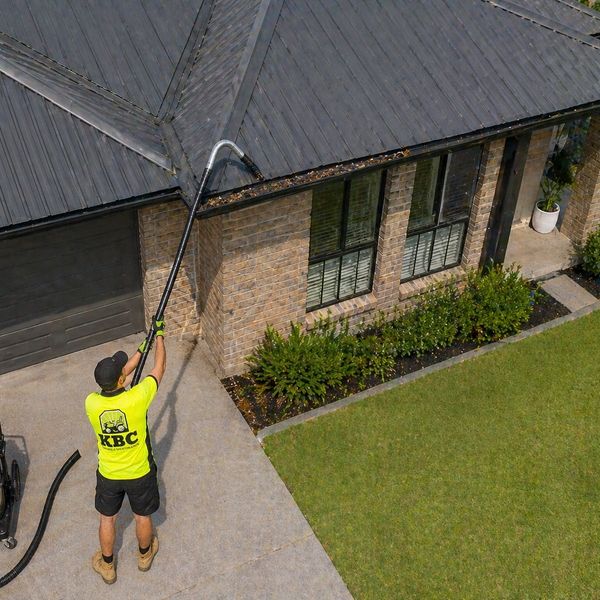A man uses a gutter vacuum to clean leaves from a roof.