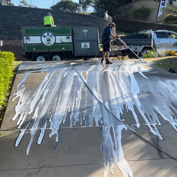 Workers cleaning a driveway with water and foam near KBC-branded equipment.