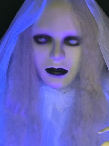 Eerie figure with pale face and dark eyes under blue light.