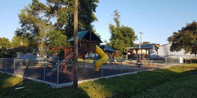 Empty playground with slides and swings enclosed by a chain-link fence on a sunny day.