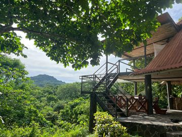 A peaceful cabin surrounded by lush green trees and hills under a blue sky.