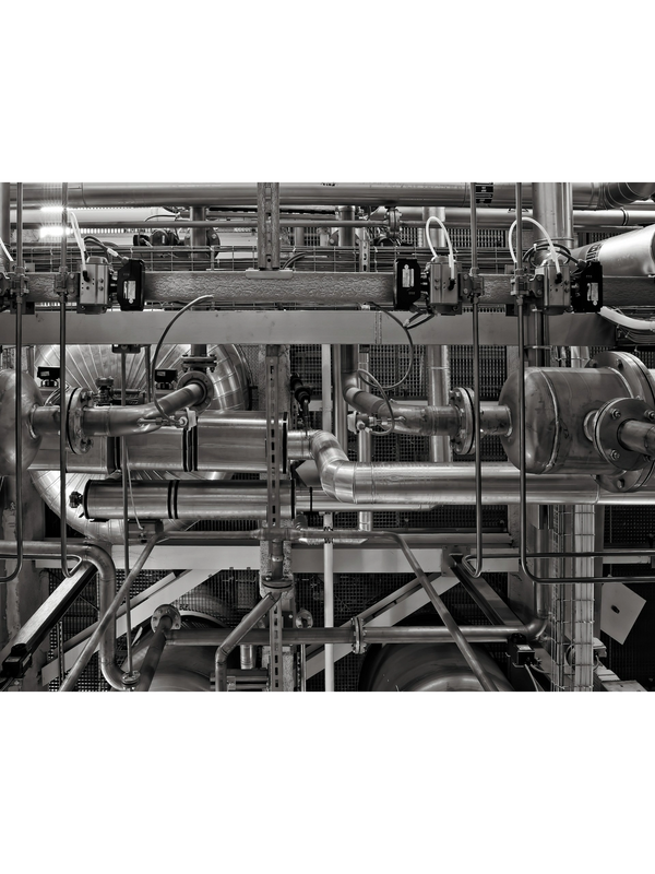 Complex network of industrial metal pipes and machinery in a factory setting.