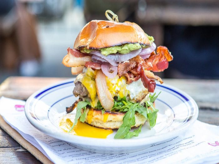 The Proper Burger® at Duke's Grocery. Shown with Applewood Smoked Bacon, Smashed Avocado & Runny Egg