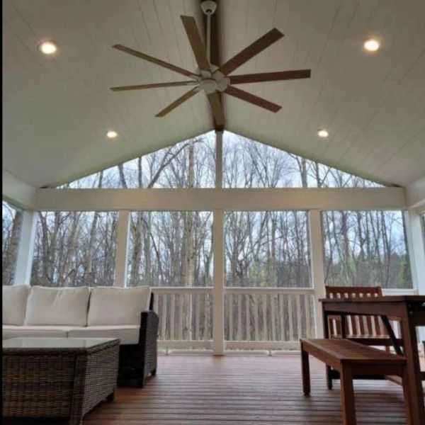 Cozy screened porch with ceiling fan and wooden furniture.