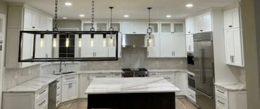 Modern white kitchen with marble countertops and stainless steel appliances.