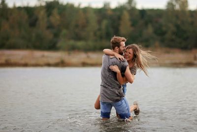 A couple joyfully embraces in shallow water outdoors.