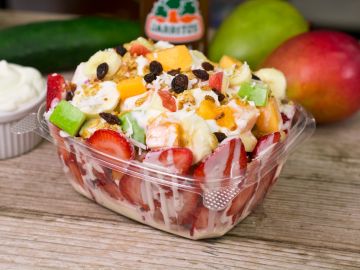 Colorful fruit salad with fresh strawberries, bananas, and raisins in a clear container.