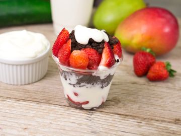 A layered dessert with strawberries, chocolate, and cream in a clear cup.