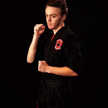 Young martial artist in black gi and black belt posing with fists up.