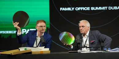 Two men hold silicon wafers while speaking at the Family Office Summit Dubai event.