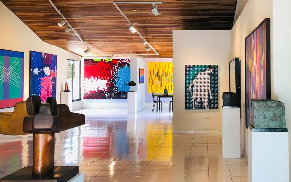 Modern art gallery with colorful paintings and sculptures under wooden ceiling.