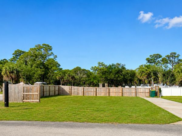 A green lawn enclosed by a wooden fence under a clear blue sky.