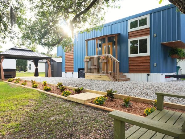 Modern blue and wood-paneled tiny house with garden and gazebo.