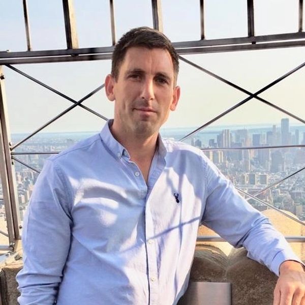 A man poses on a high observation deck with a city skyline in the background.