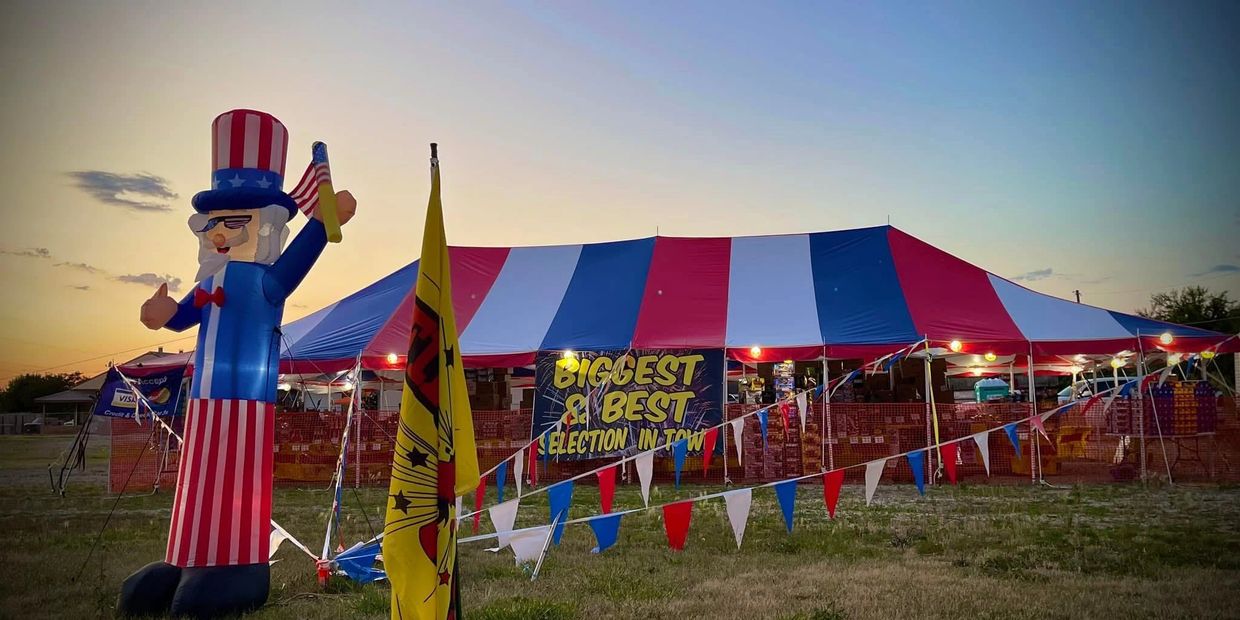 Large patriotic tent with Uncle Sam inflatable and colorful flags at dusk.
