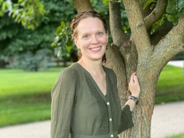 Woman smiling while standing by a tree in a park.