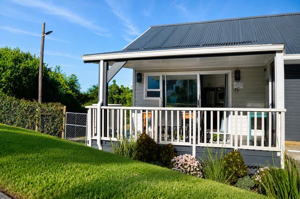Cozy house porch with white railing and lush greenery.