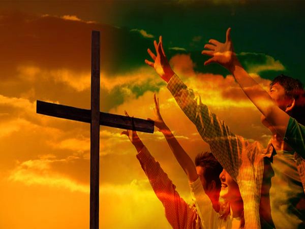 People raising hands in praise near a cross at sunset.