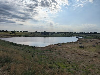 A calm pond surrounded by grassy fields under a partly cloudy sky.