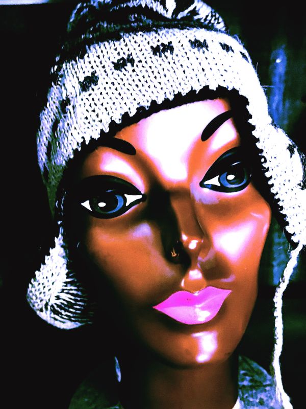 Close-up of a mannequin head wearing a knitted hat with bold makeup.