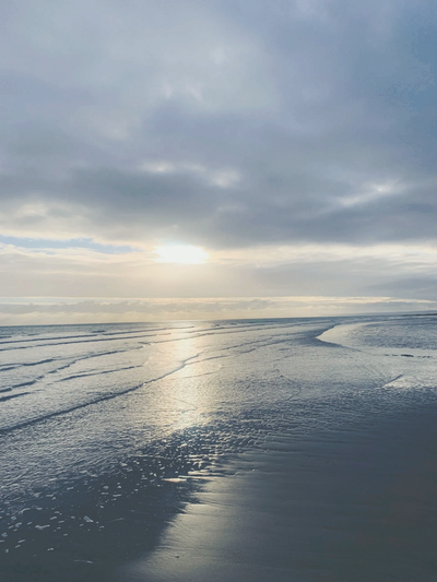 Sunset casting reflections on calm beach waters under a cloudy sky.