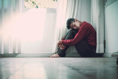 Man sitting on floor near a window hugging his knees