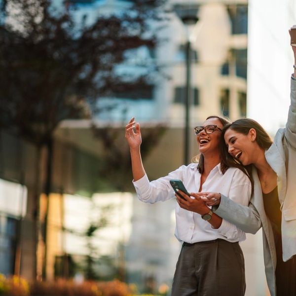 Two women joyfully laughing and celebrating outdoors in a city setting.