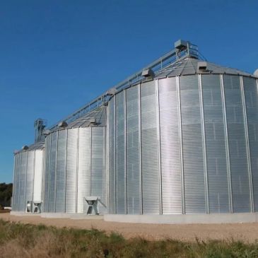 Large metal grain silos under clear blue sky.